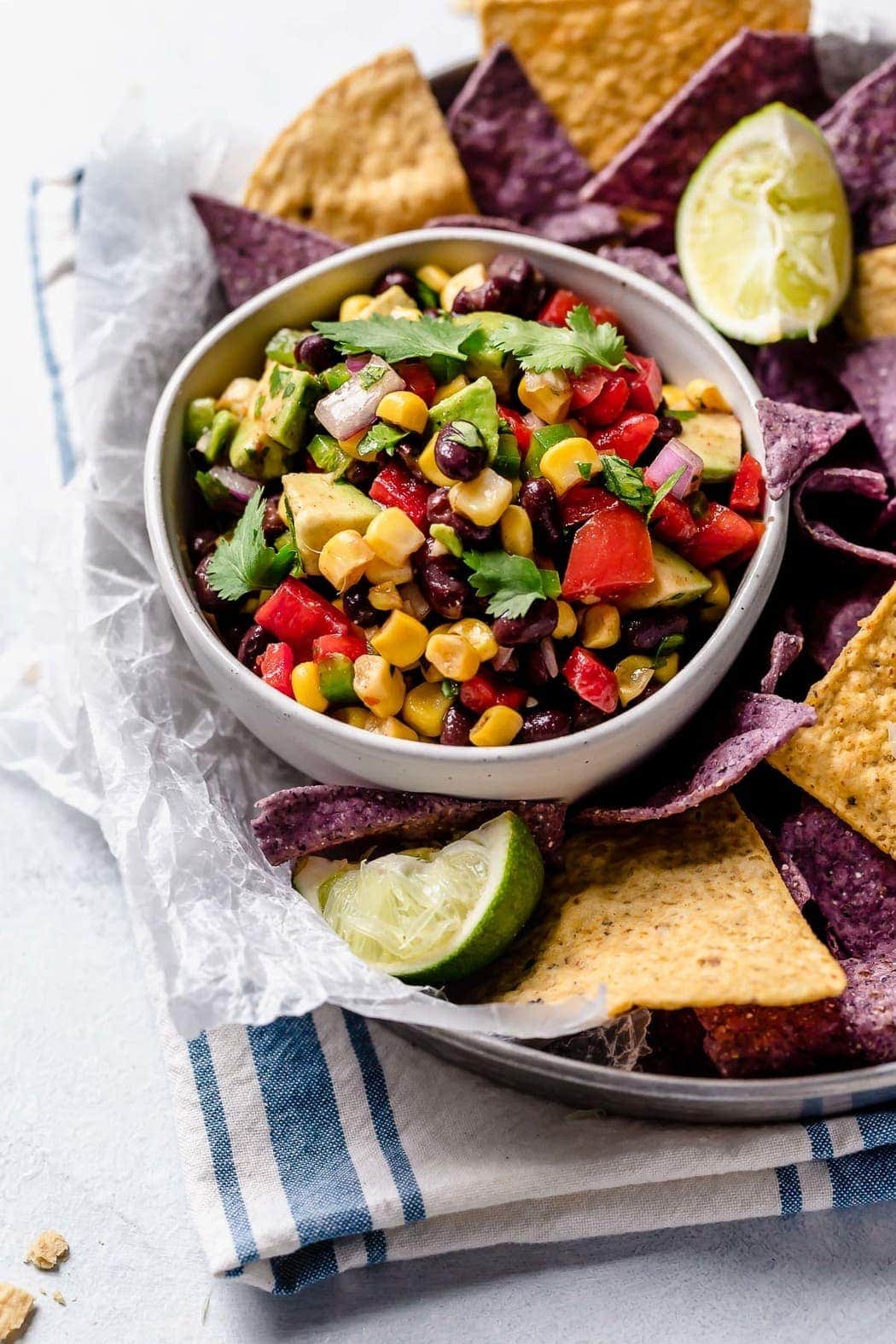 Black Bean & Corn Salsa with Avocado in a white bowl surrounded by blue and white corn tortilla chips.