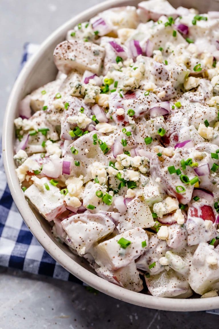 Close up view of a serving bowl filled with blue cheese potato salad topped with chives and crumbled blue cheese. 