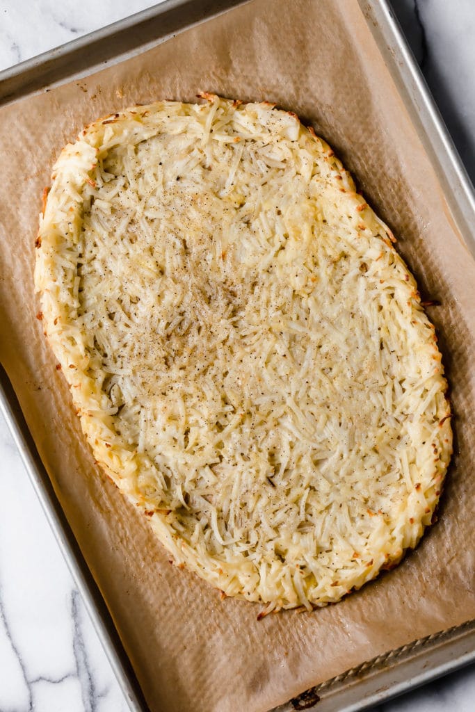 Overhead of hash brown crush for the breakfast pizza on a baking sheet after it has been baked.