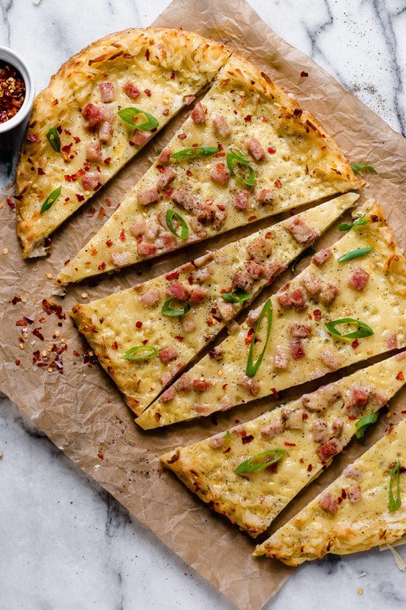 Overhead photo of Breakfast Pizza with Hash Brown Crust topped with green onion slices and crushed red pepper. Sliced into 6 triangles. 