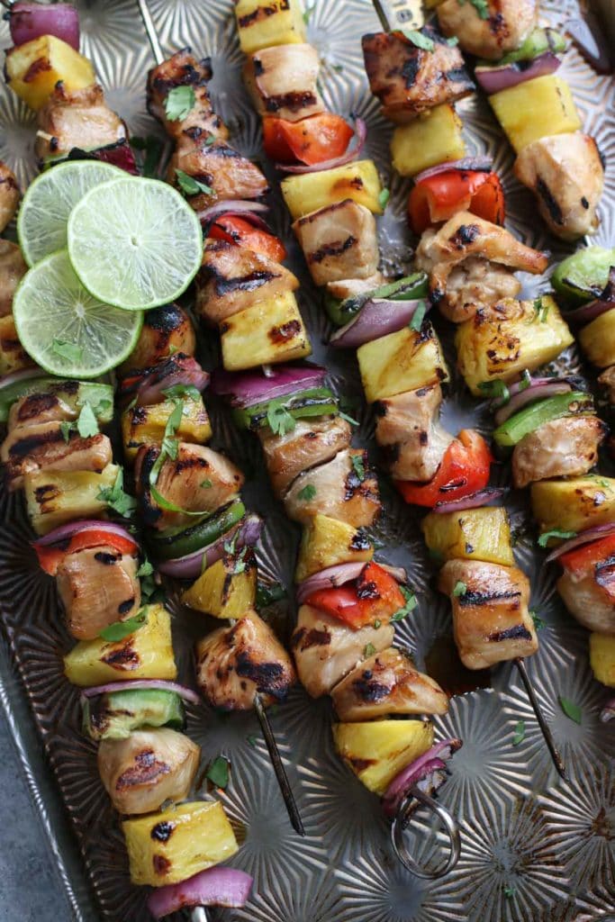 Chicken kebabs with peppers, pineapple, and onions with lime slice garnish on baking sheet.