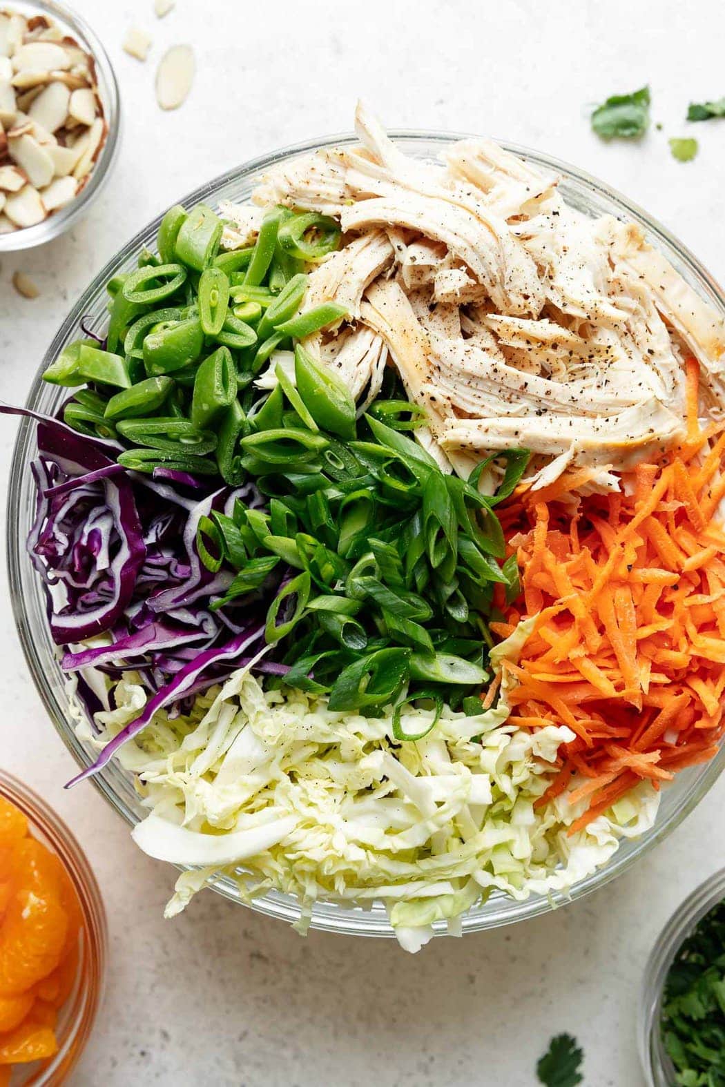 Overhead view of ingredients for Chinese chicken salad in a large clear bowl ready to be tossed together.