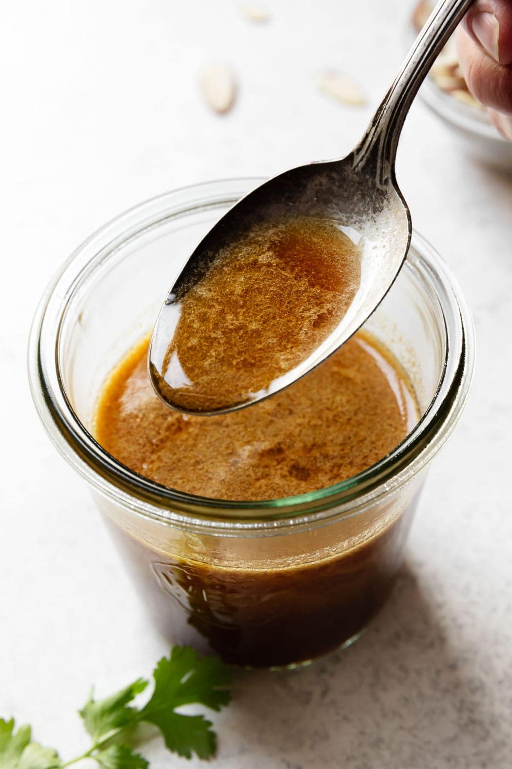 A small glass jar of homemade sauce for Chinese chicken salad with a spoonful of sauce to show chinese-inspired color.