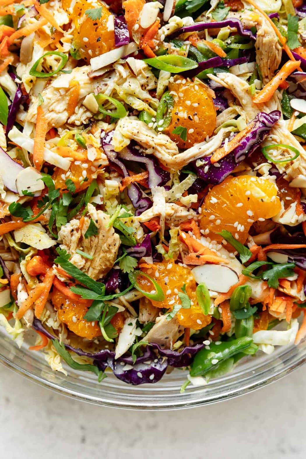 A close up view of Chinese-inspired chicken salad with shredded chicken, shredded cabbage, snap peas, and toasted almonds in a serving bowl sprinkled with sesame seeds. 