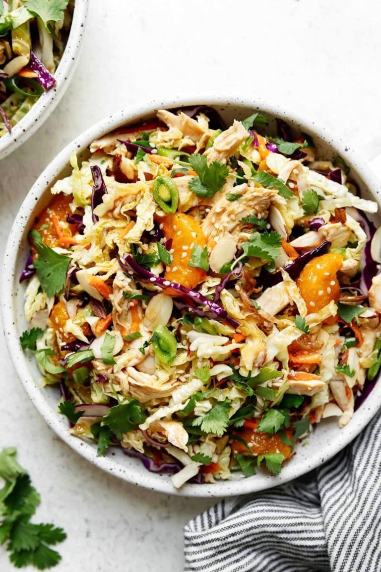 Overhead mandarin orange chicken salad in white bowl packed with crisp-crunchy veggies, toasted nuts, tender chicken, sweet oranges, and delicious sesame-ginger sauce. 