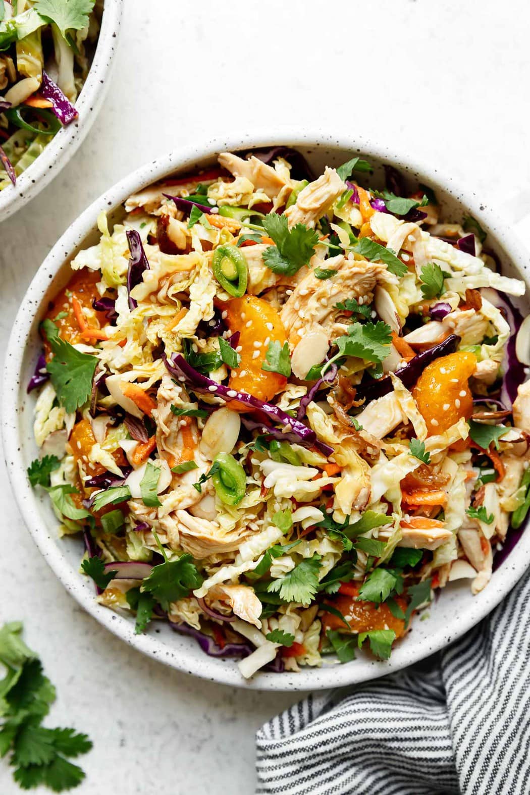 A big bowl of Chinese chicken salad topped with fresh herbs, purple cabbage, and mandarin oranges.