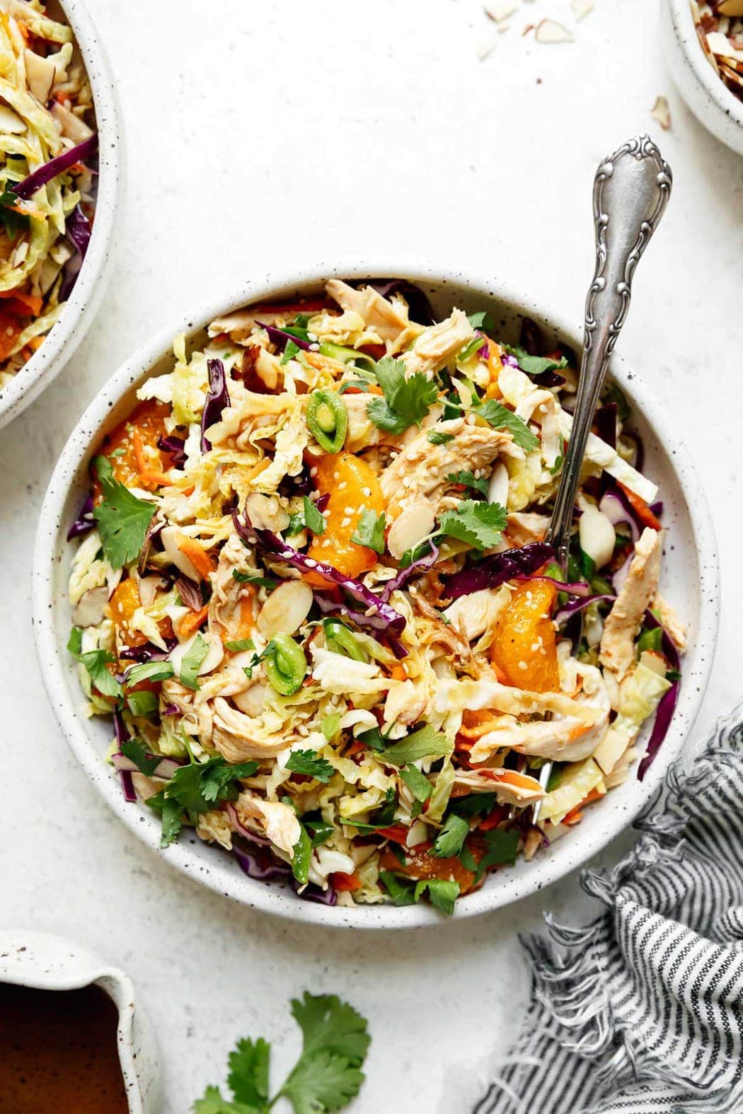 A large bowl filled with Chinese-Inspired chicken salad topped with sliced snap peas, purple cabbage shreds, sesame seeds, and orange slices.