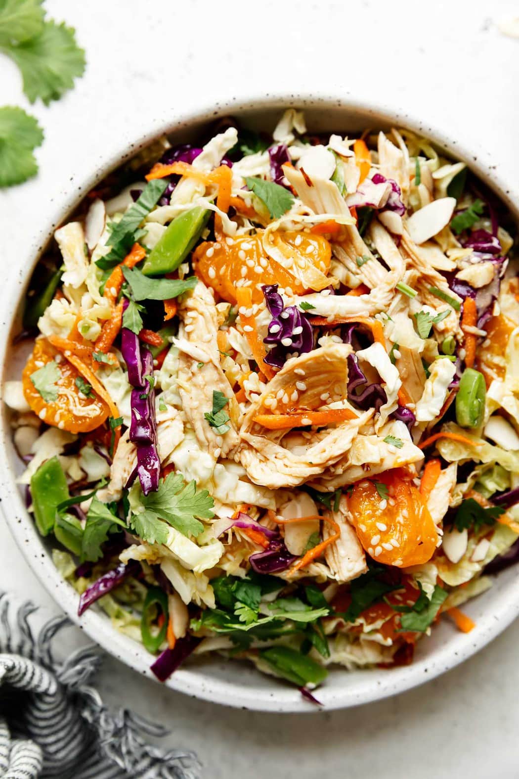 Overhead view of Chinese chicken salad topped with chicken, sesame seeds, purple cabbage, and mandarin oranges.