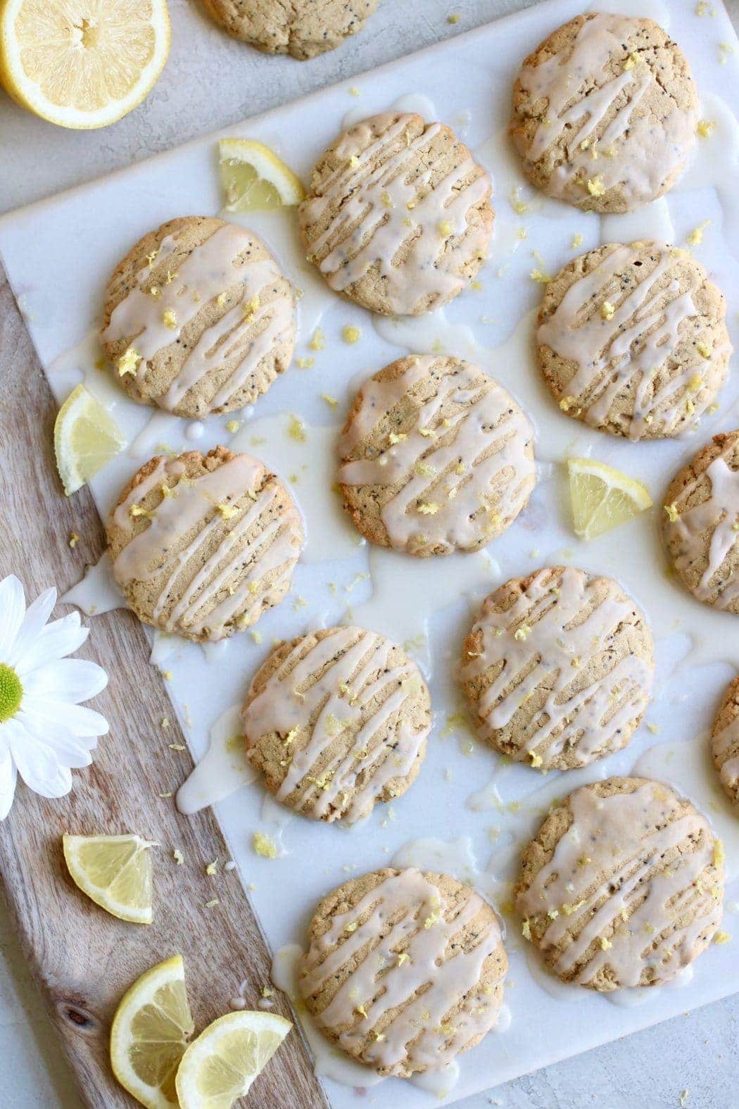 Overhead shot of the Paleo Lemon Poppy Seed Cookies single layered on a white marble cheese board and drizzled with a glaze and sprinkled with lemon zest.
