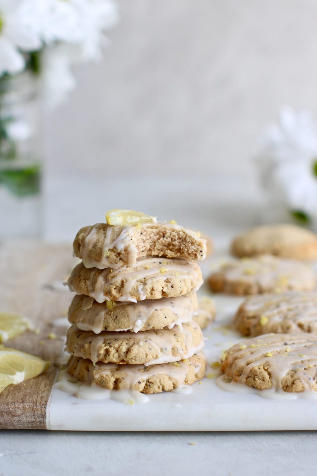 Photo of a stack of five Paleo Lemon Poppy Seed Cookies drizzled with a glaze. The top cookie has a perfect bite out of it.