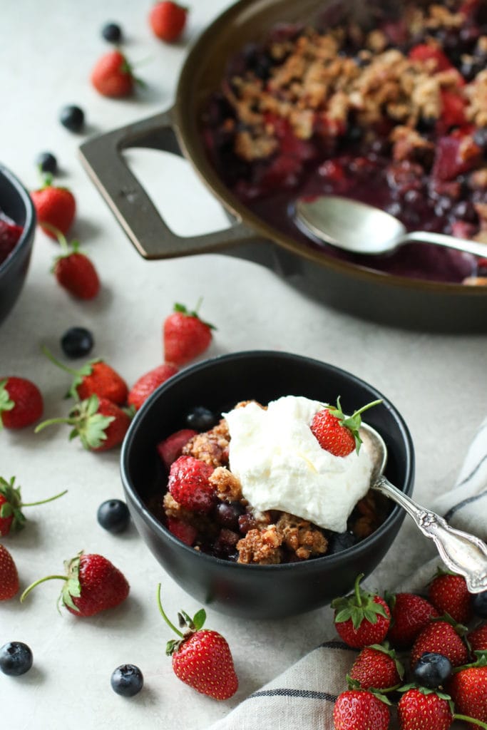 Bowl and cast-iron skillet filled with berry crisp and berries scattered around