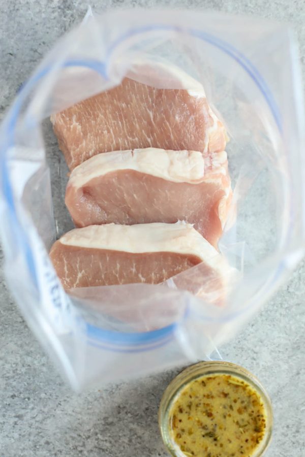 Gallon zip-top plastic bag with raw pork chops and a jar of one of the 5 Easy Pork Marinades. 