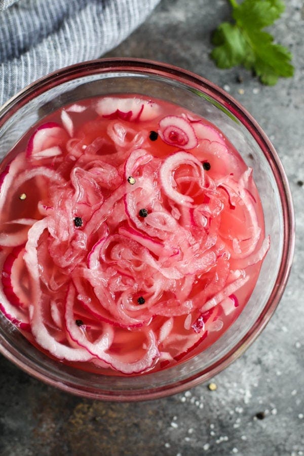 Close up view of red onions soaking in apple cider vinegar in a clear mixing bowl for quick pickled onions.