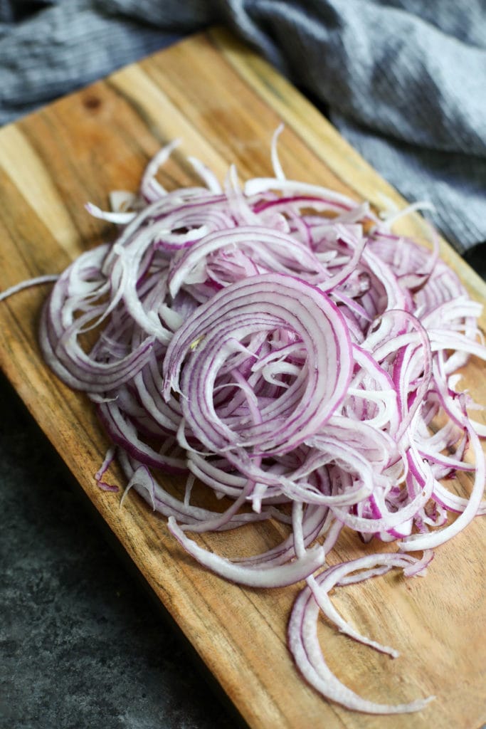 Red onions cut into strands on a wooden cutting board