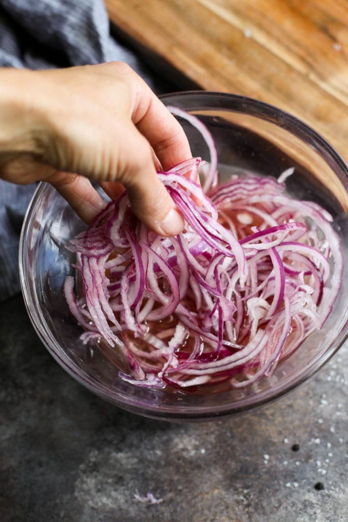 Red onion strands being put into a bowl filled with pickle mixture to begin soaking.
