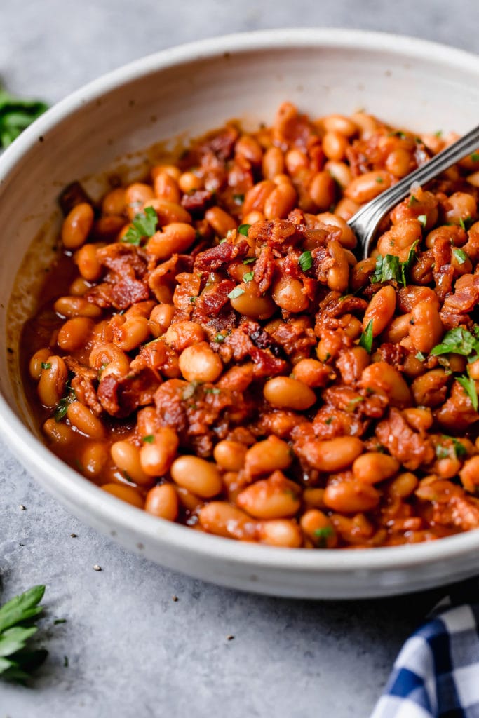 Bowl of baked beans with bacon with a spoon scooping some out with green garnish