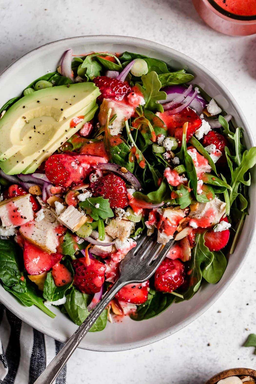 Close up overhead view strawberry spinach salad in stone bowl, topped with chicken and avocado slices.