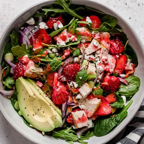 Overhead view bowl filled with strawberry spinach salad topped with avocado and strawberry vinaigrette.