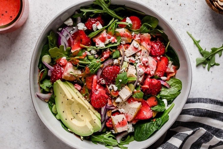 Overhead view bowl filled with strawberry spinach salad topped with avocado and strawberry vinaigrette.