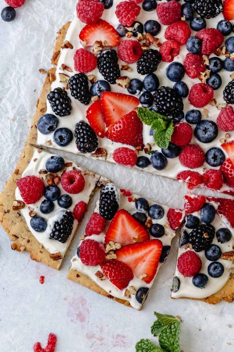 Overhead view of a colorful berry fruit pizza topped with a variety of berries and garnished with mint leaves.