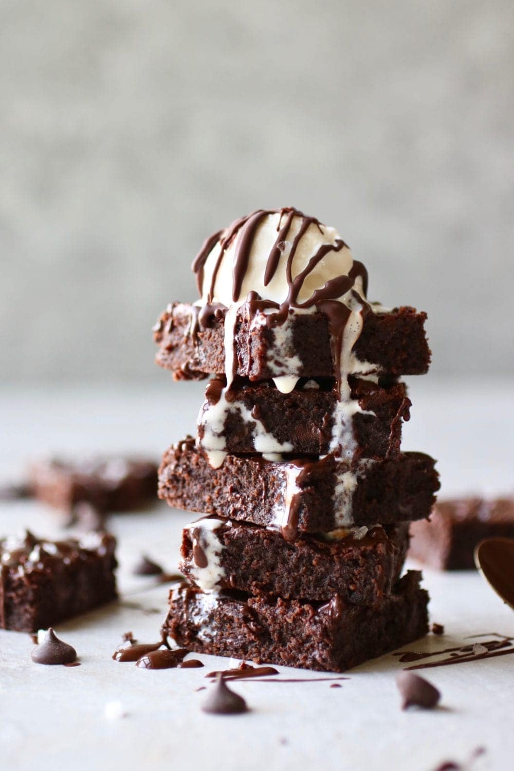 Photo of a stack of five Paleo Fudgy Brownies with a scoop of cream on top. Drizzled with chocolate. 