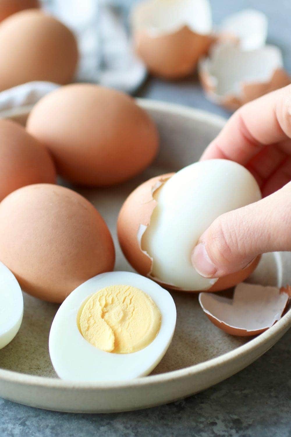 A hard-boiled egg being removed from the brown shell on a plate along with brown eggs and a hard-boiled egg cut in half. 