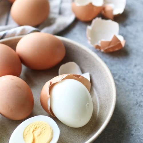 Easy peel hard-boiled eggs in a low bowl, some freshly peeled and sliced in half.