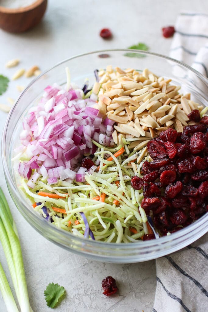 All ingredients in clear glass mixing bowl for creamy ranch broccoli slaw.