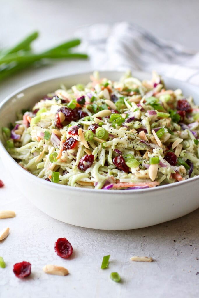 Side view ranch broccoli slaw with dried cranberries and toasted almonds in white bowl.