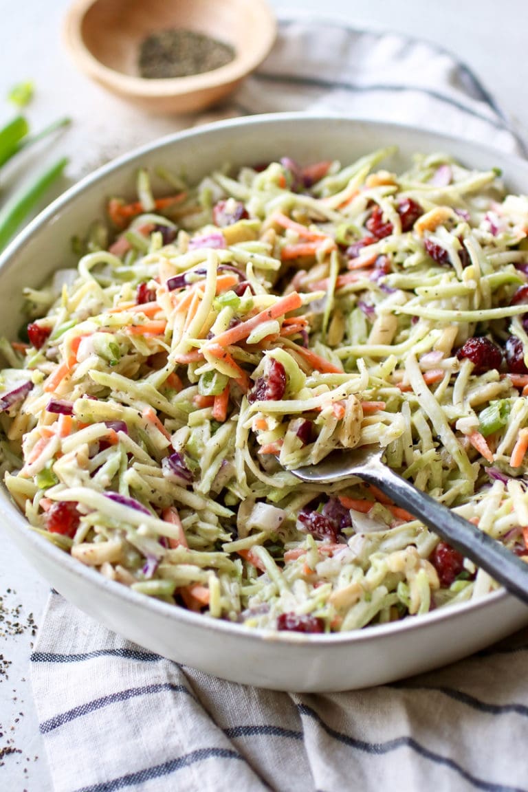 Close up view of a serving bowl filled with creamy ranch broccoli slaw topped with toasted almonds and dried cranberries. 