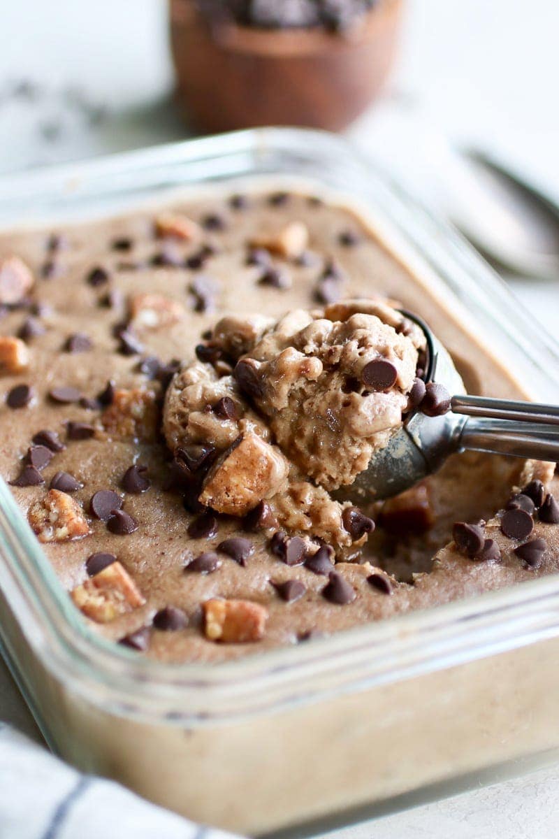 Photo of Almond Butter Banana Nice Cream served in a glass contain topped with chocolate chips and pieces of Caveman Collagen Bar. Picture shows an ice cream scoop holding a scoop of the nice cream.