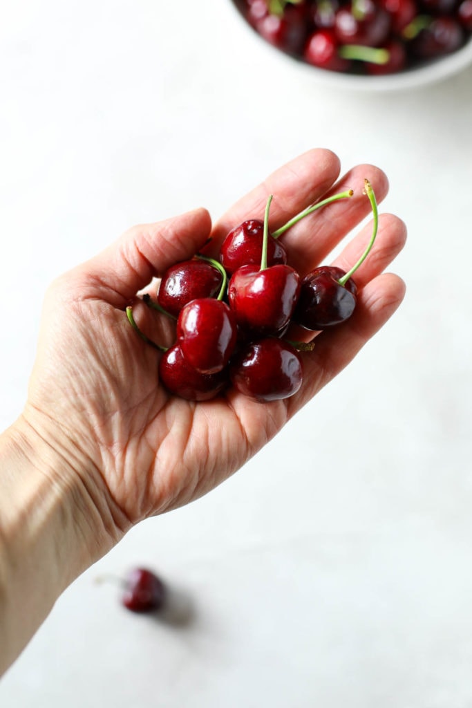 Hand extended with multiple cherries in the hand.