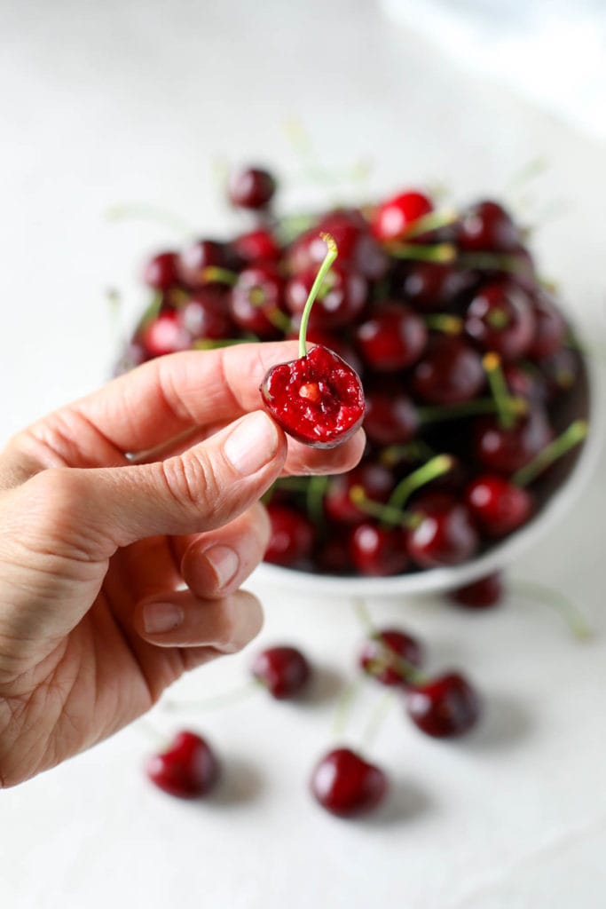 Inside view of a cherry with stem on it with a bowl of fresh cherries in the background.
