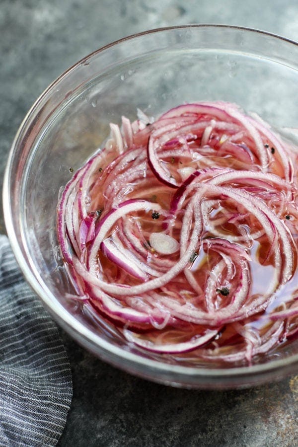 Close up view of quick pickled red onions soaking in a clear mixing bowl.