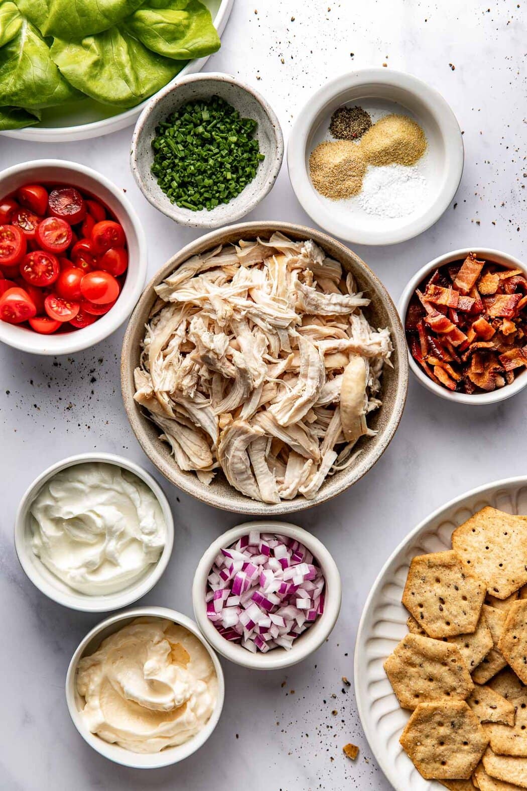 Overhead view of a variety of ingredients for BLT Chicken Salad in different sized bowls. 