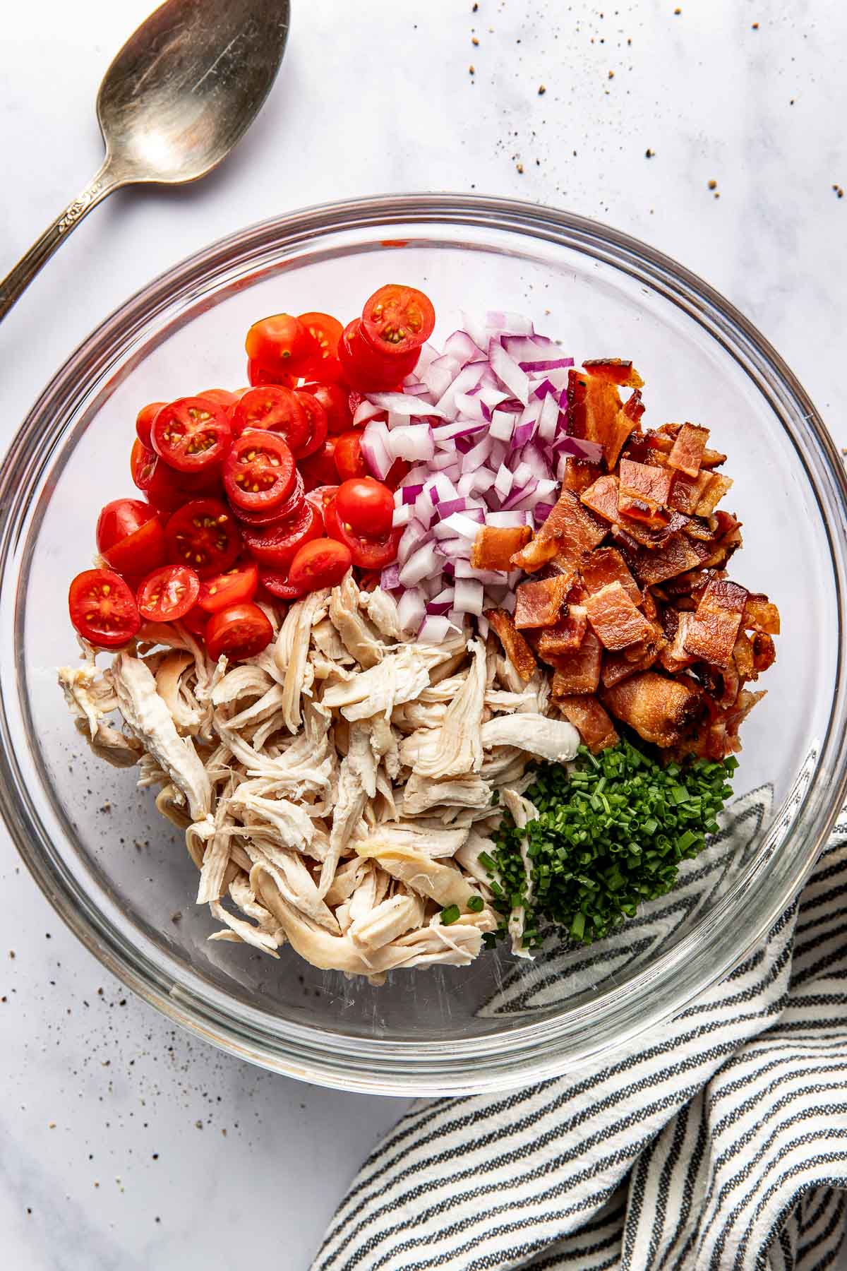Overhead view of a glass bowl filled with salad ingredients including shredded chicken. 