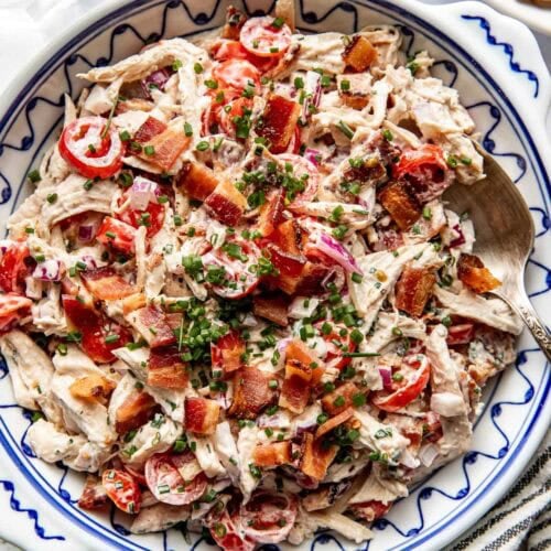 Overhead view of a serving bowl filled with BLT Chicken Salad topped with crisp bacon pieces and chives.