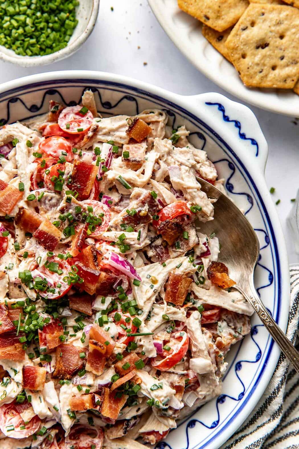 Close up view of a bowl of BLT Chicken Salad topped with fresh chives and crackers on the side. 