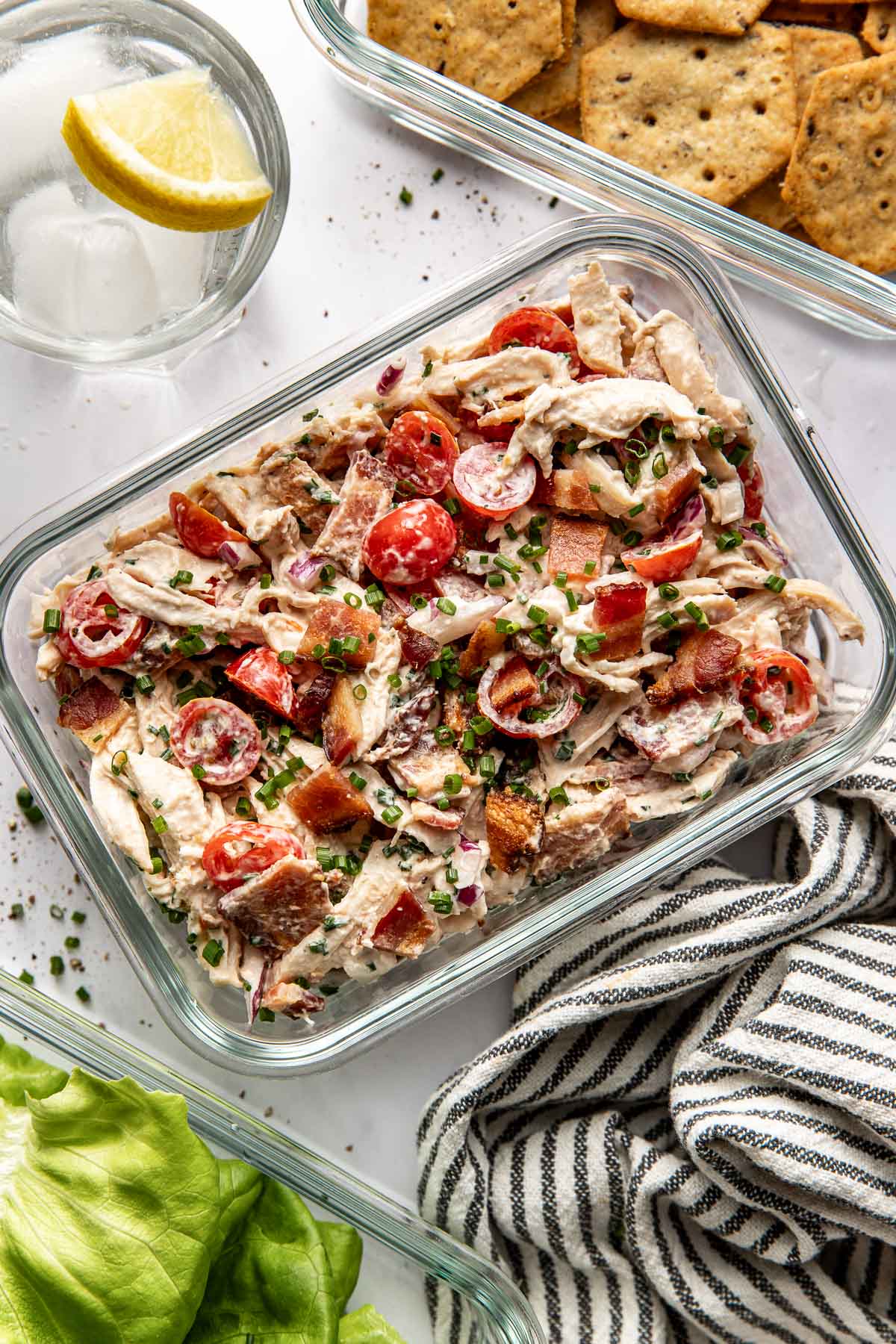 Overhead view of a glass meal prep container filled with BLT Chicken Salad topped with fresh chives. 