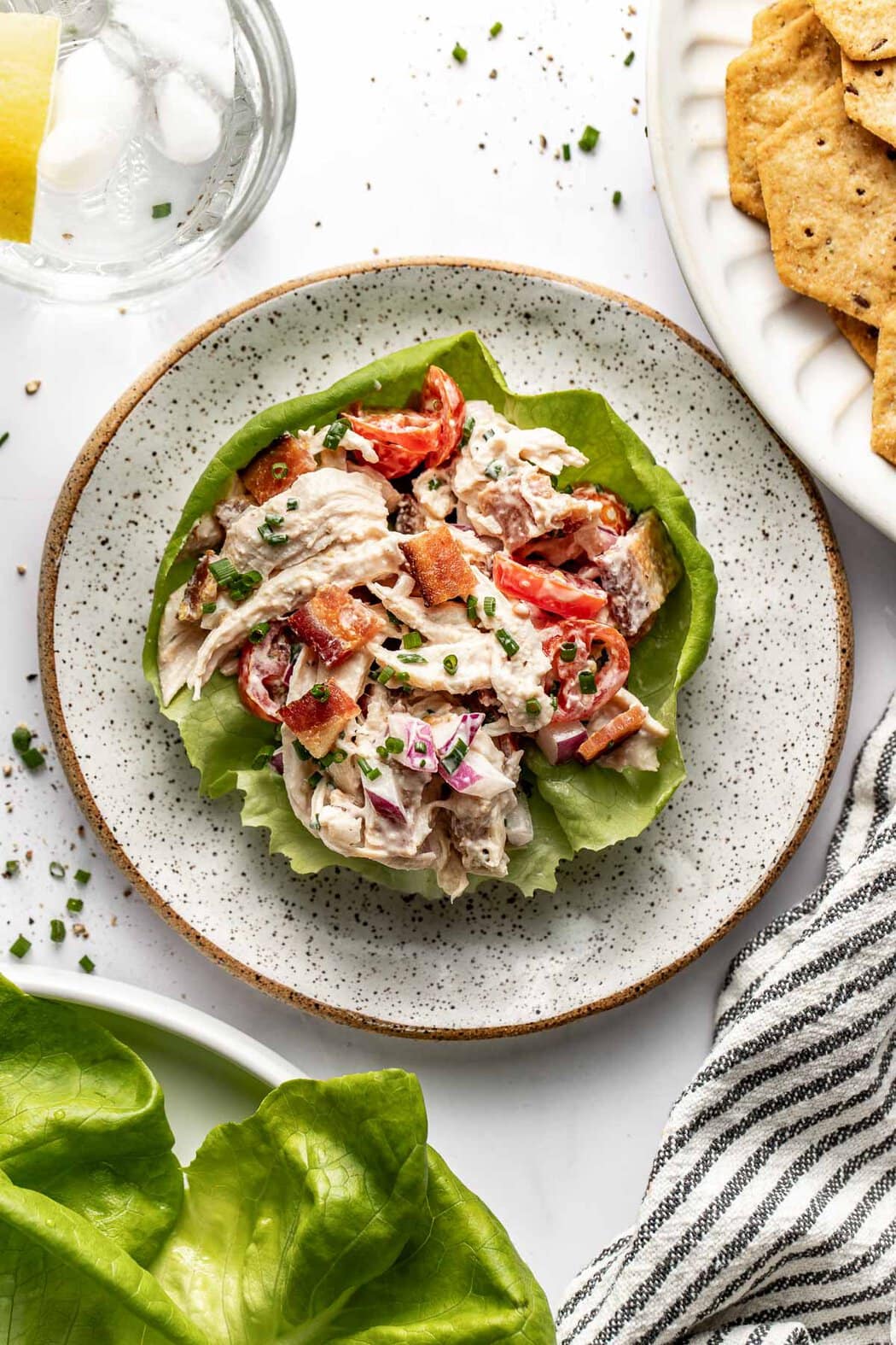 Overhead view of a lettuce leaf on a plate topped with BLT Chicken Salad and fresh chives. 