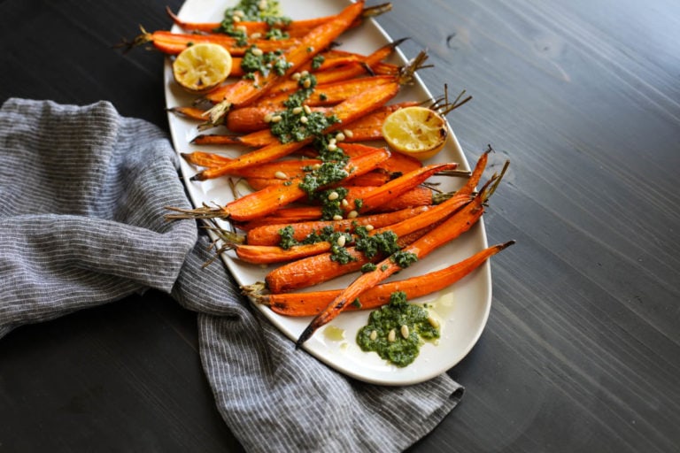 Roasted whole carrots on serving platter topped with pesto