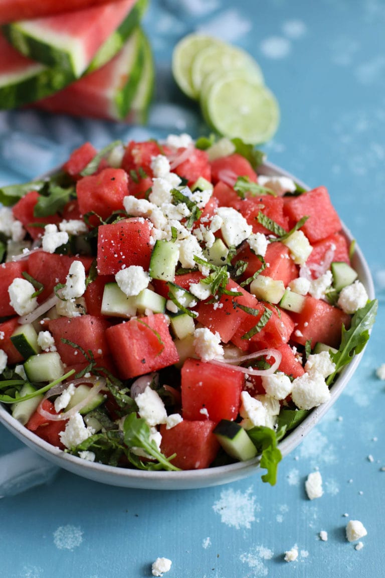 Close up view of a bowl of watermelon and feta salad topped with fresh herbs and tart lime juice. 