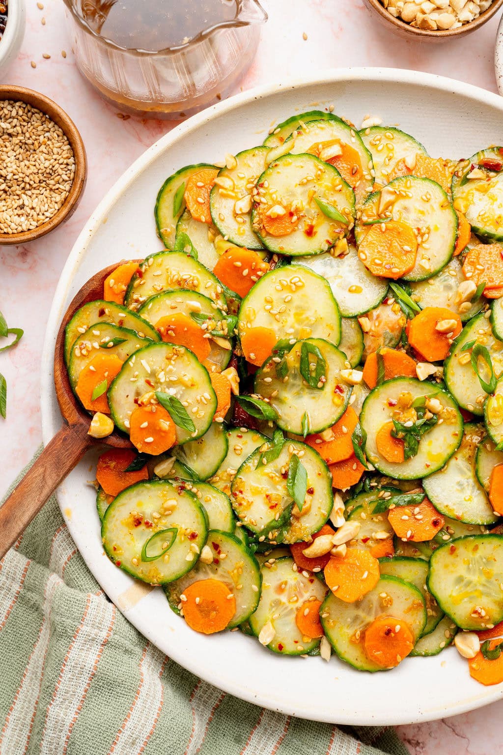 Overhead view of a plate of Asian Cucumber Salad topped with sesame seeds, green onions, and peanut pieces.