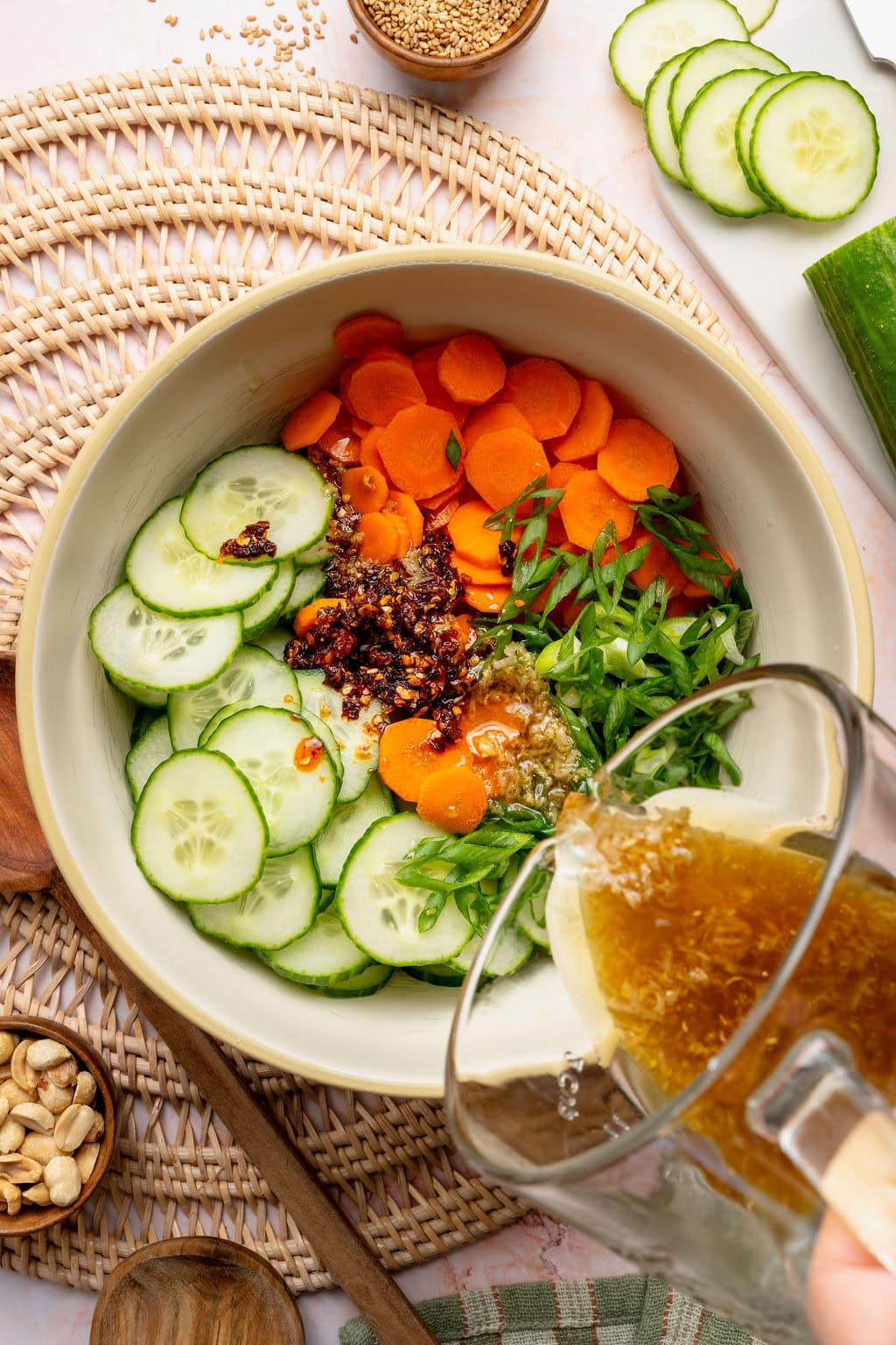 Overhead view of a bowl of Asian Cucumber Salad with the ingredients arranged in sections with and Asian dressing being poured over the top.