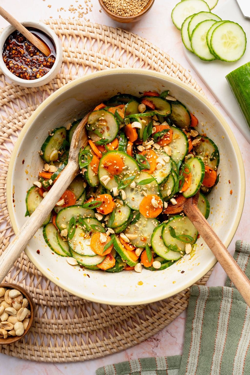 Overhead view of a bowl of Asian Cucumber Salad being tossed with two wooden spoons.