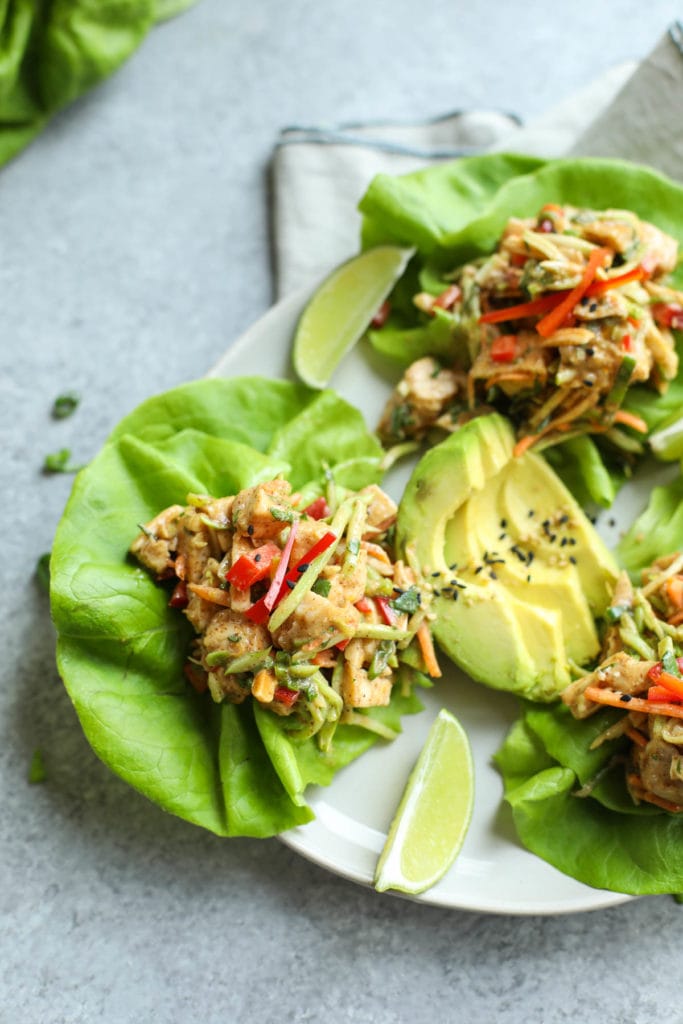 Asian chicken salad served on lettuce leaves on small plate with avocado and lime garnish