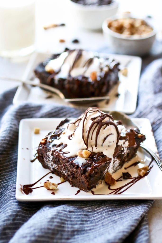 Slow Cooker Pumpkin Brownies plated on square white plate topped with melty vanilla ice cream and drizzled with chocolate.