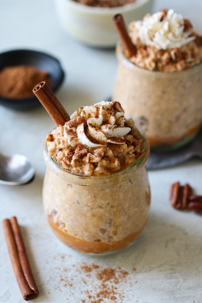 Pumpkin Pie Overnight Oats in small jars topped with whipped cream and cinnamon stick.