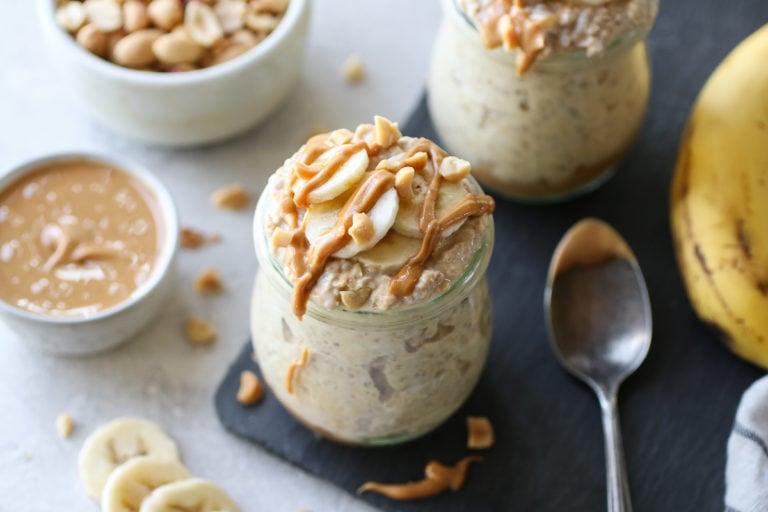 Close up view of Peanut Butter Banana Overnight Oats in glass jar topped with sliced bananas, peanuts, and drizzled with peanut butter. 