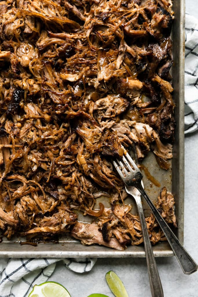 Close up view of shredded pork shoulder in a baking sheet for slow cooker carnitas recipe. 